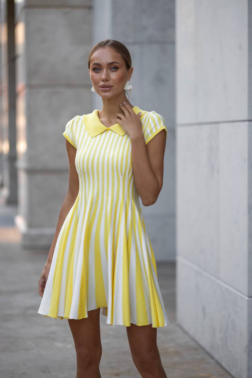 Woman wearing a yellow and white striped dress standing against a gray wall.