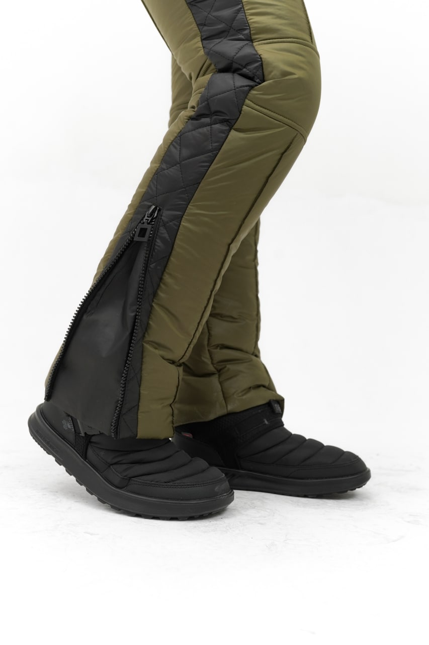 Green pants with black zippers and black shoes on a white background