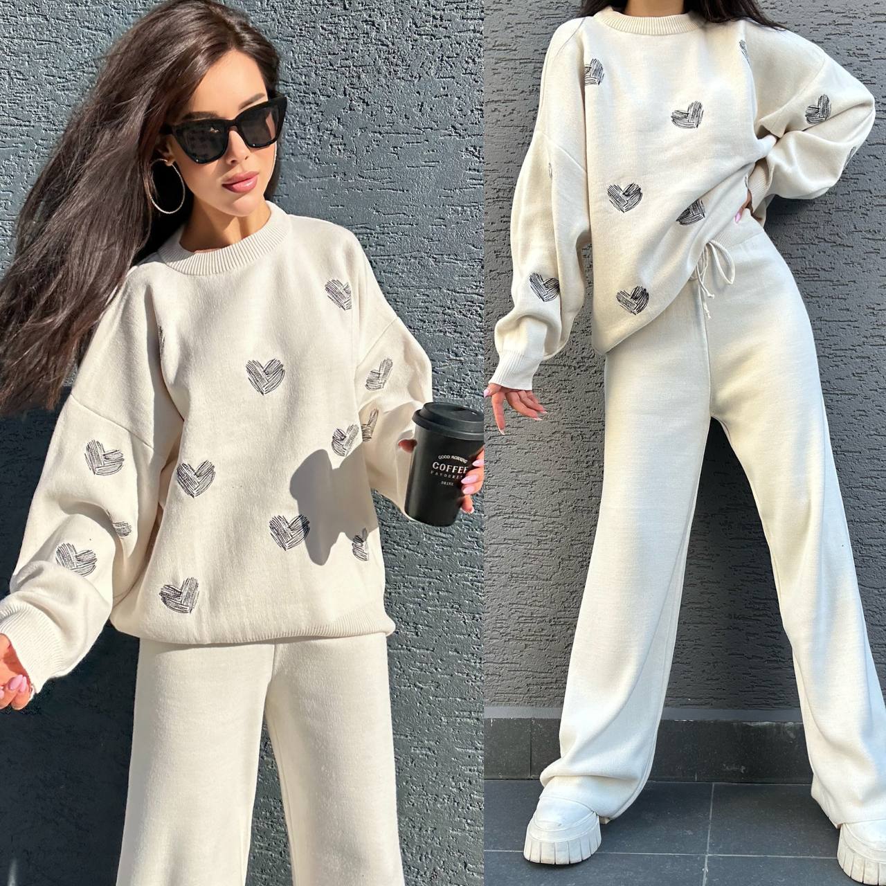 Woman wearing a white outfit with heart patterns, holding a coffee cup against a gray wall.