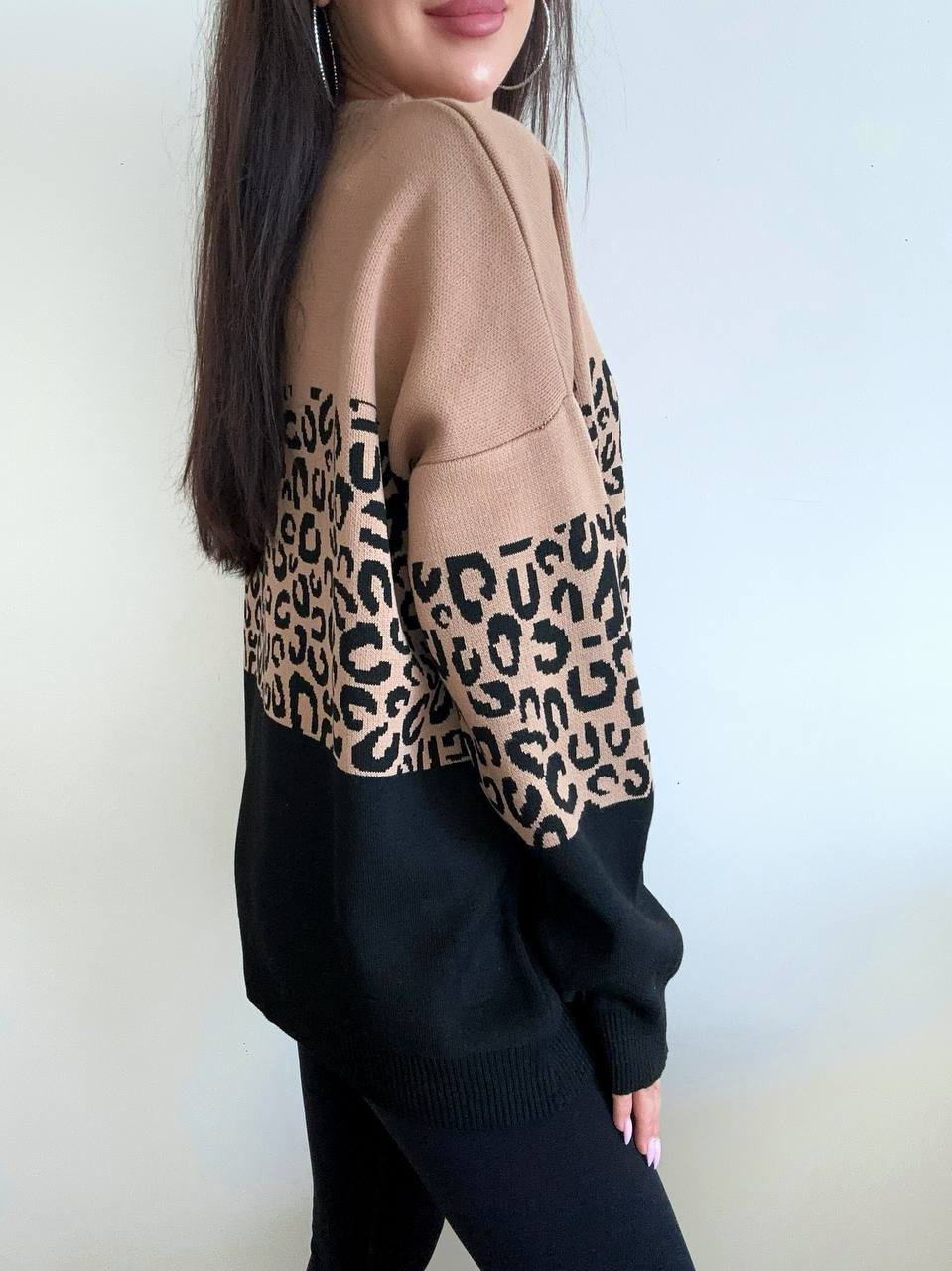 Person wearing a sweater with leopard print sleeves against a plain background