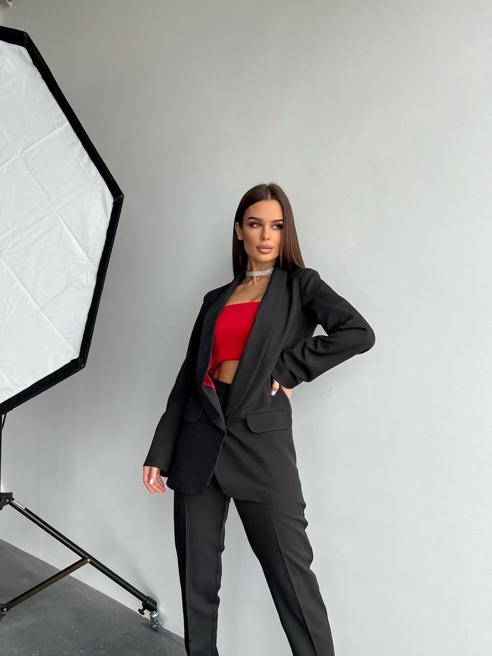 Woman in a black suit with a red top standing in front of a photography studio light.