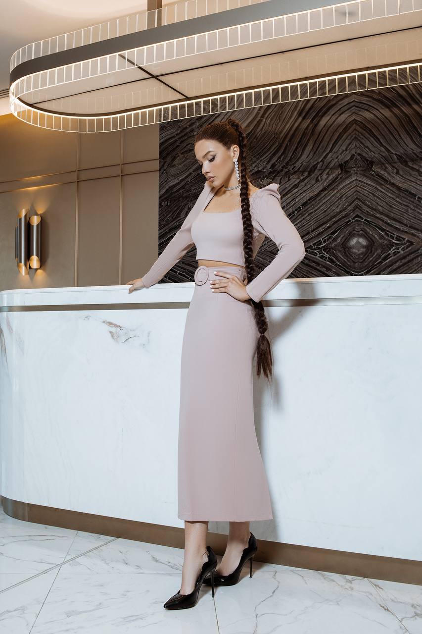 Woman in a light pink outfit standing in a modern interior setting.