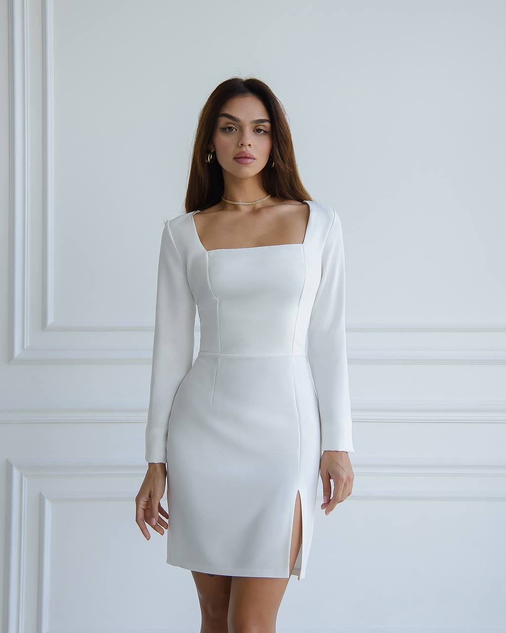 Woman wearing a white dress with long sleeves against a white wall