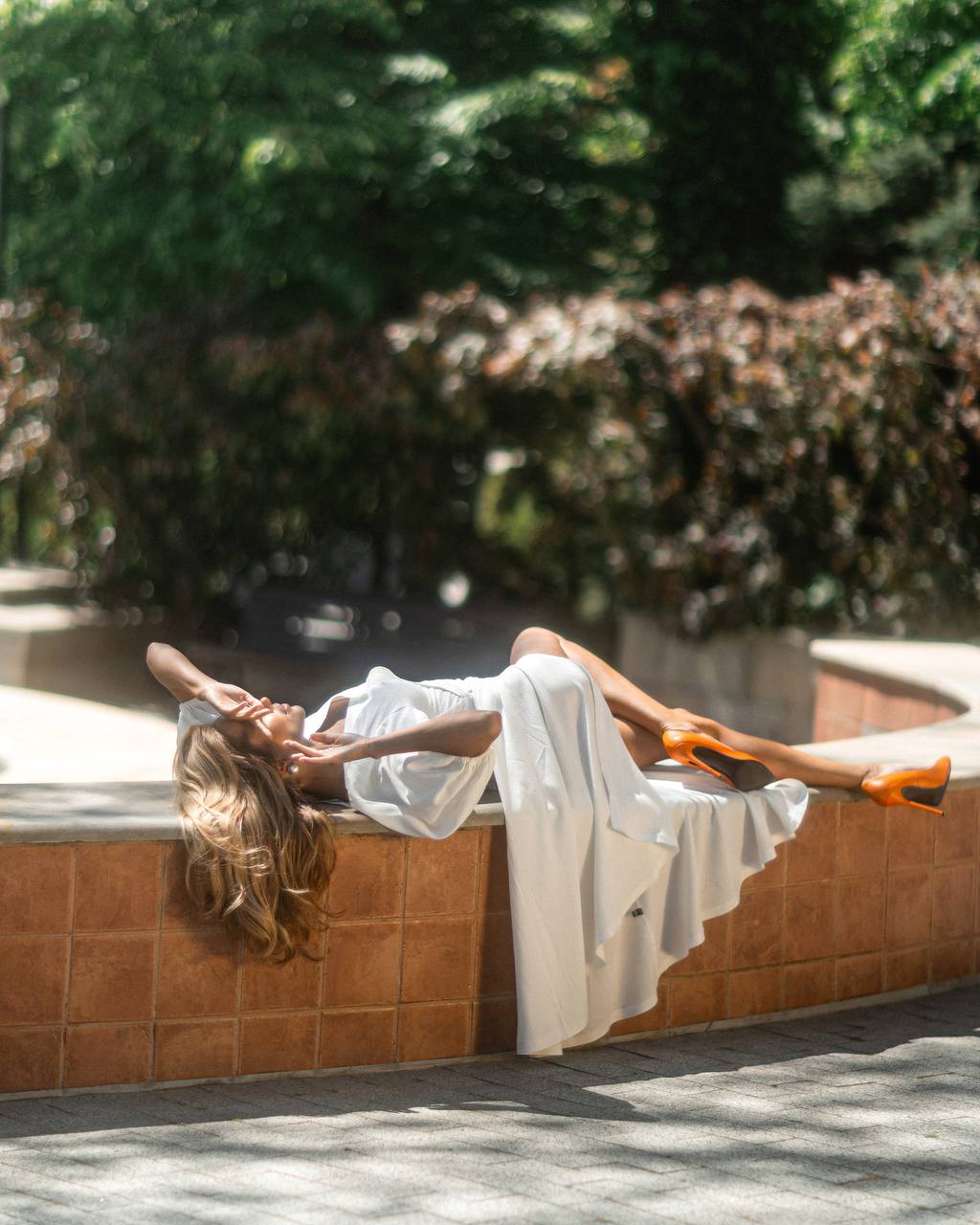 Woman in a white dress lying on a stone ledge with greenery in the background