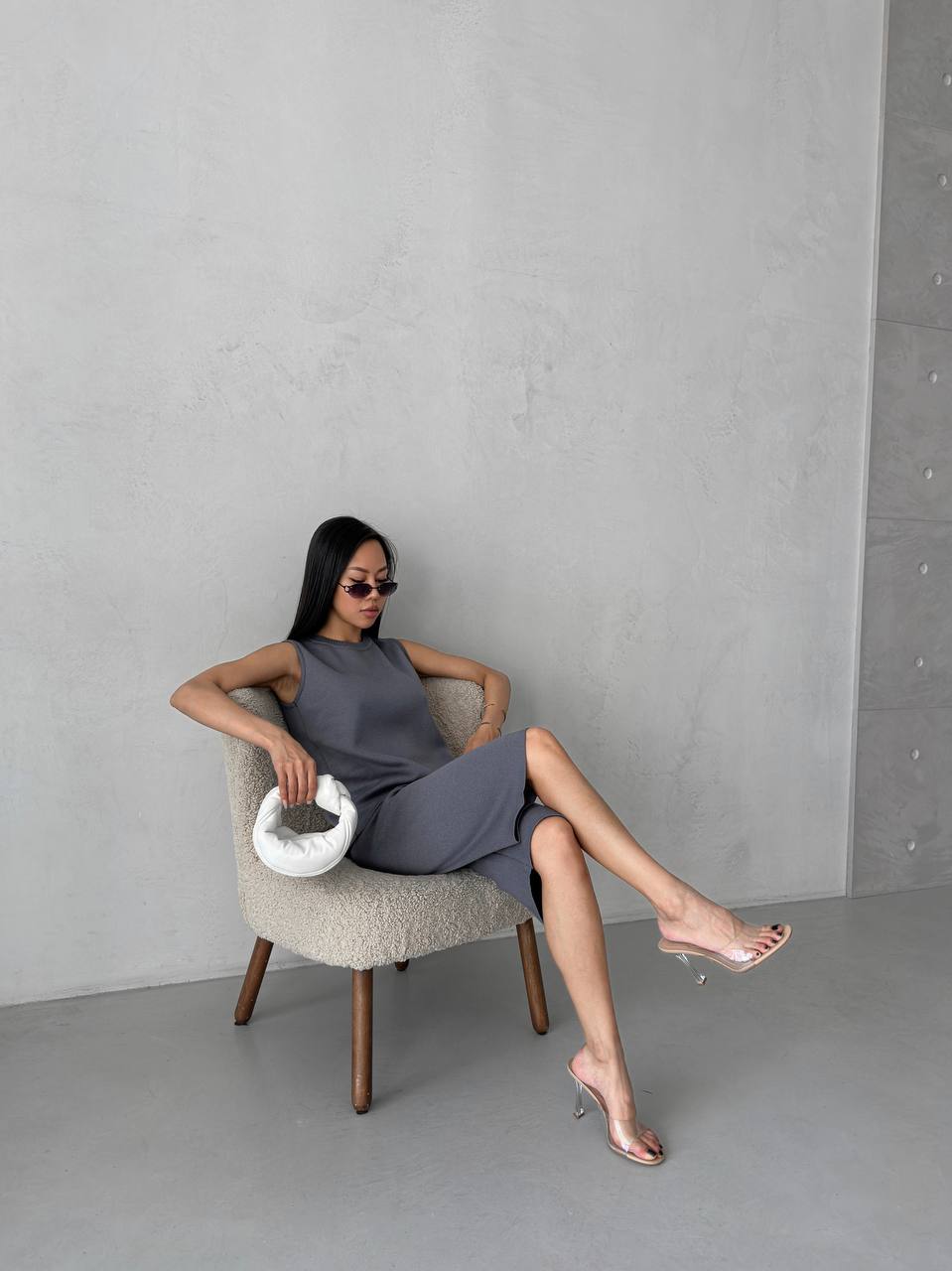 Woman sitting on a chair holding a white bag against a gray wall.
