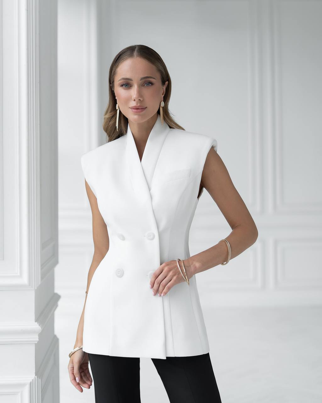 Woman wearing a white sleeveless blazer against a light-colored wall.