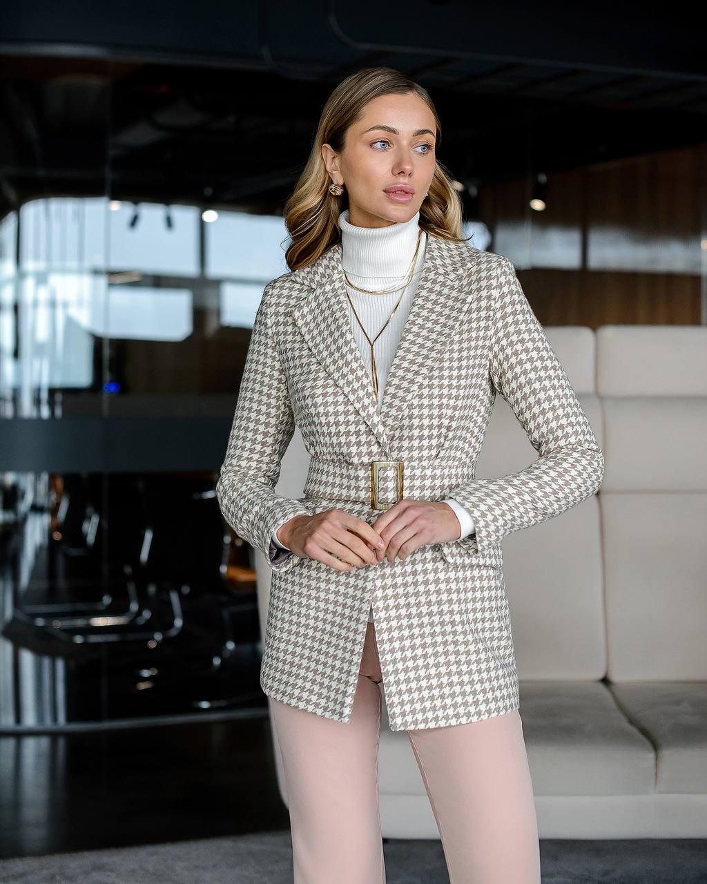 Woman in a houndstooth blazer and shorts standing in an indoor setting.