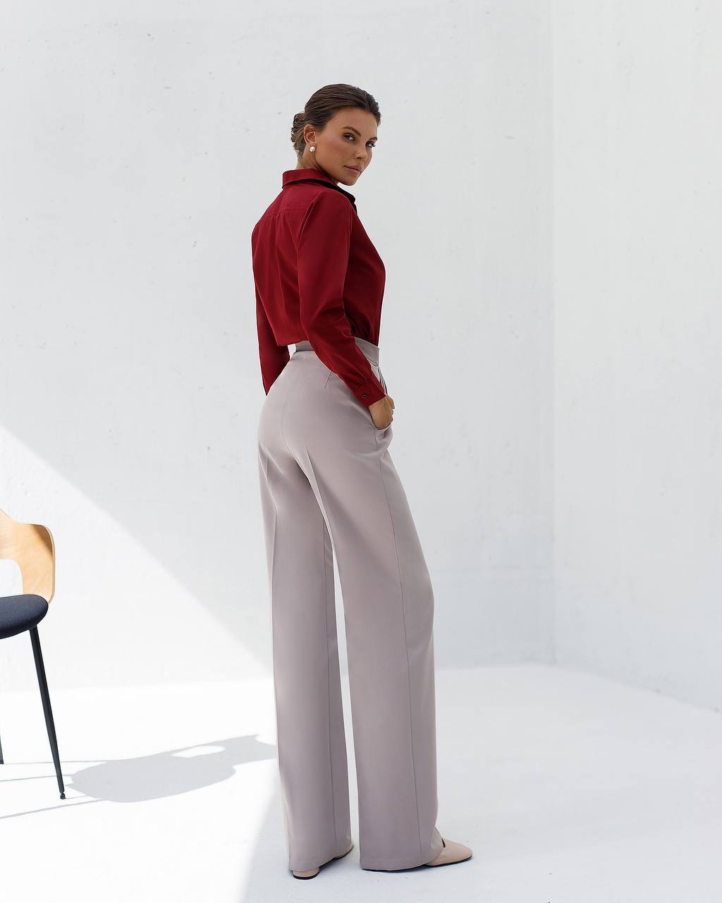 Woman wearing a red blouse and light gray pants on a white background