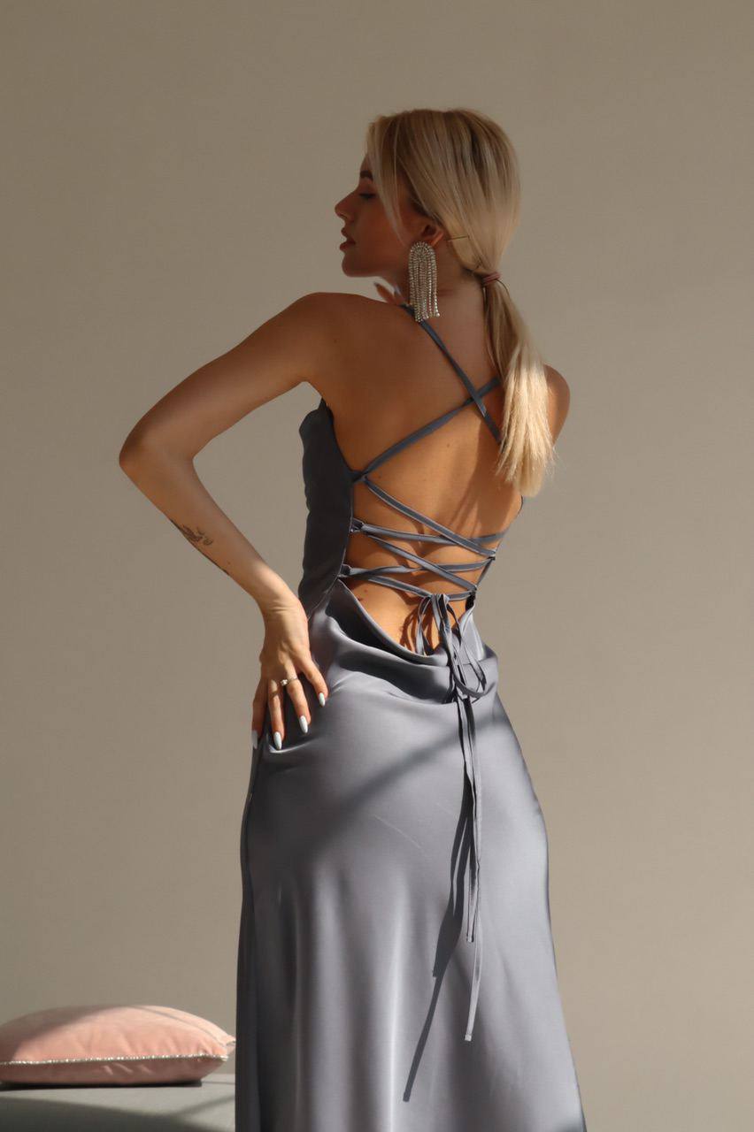 Woman wearing a strappy top and gray pants against a beige background