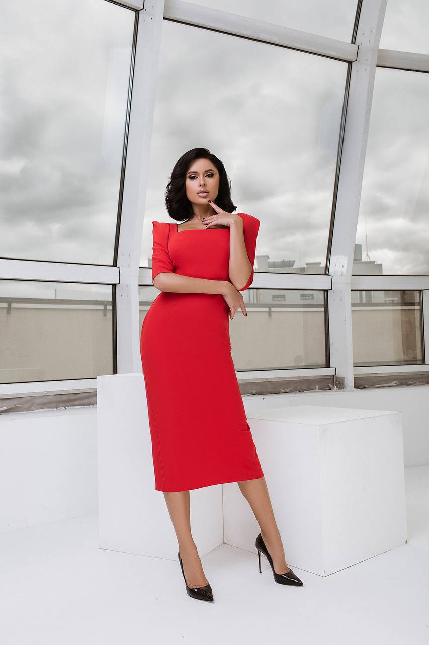 Woman in a red dress standing in front of a modern glass structure.