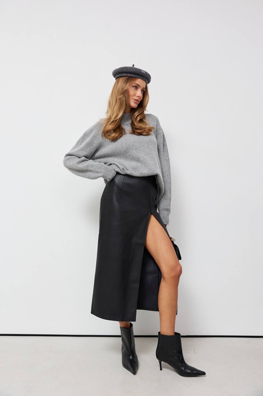 Woman wearing a gray sweater, black leather skirt, and black boots against a white background