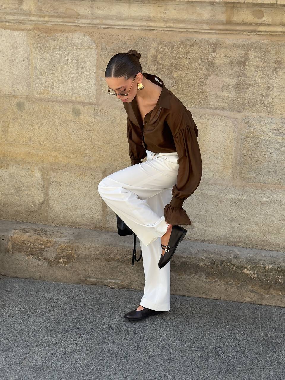 Woman in brown blouse and white pants sitting on a stone wall.