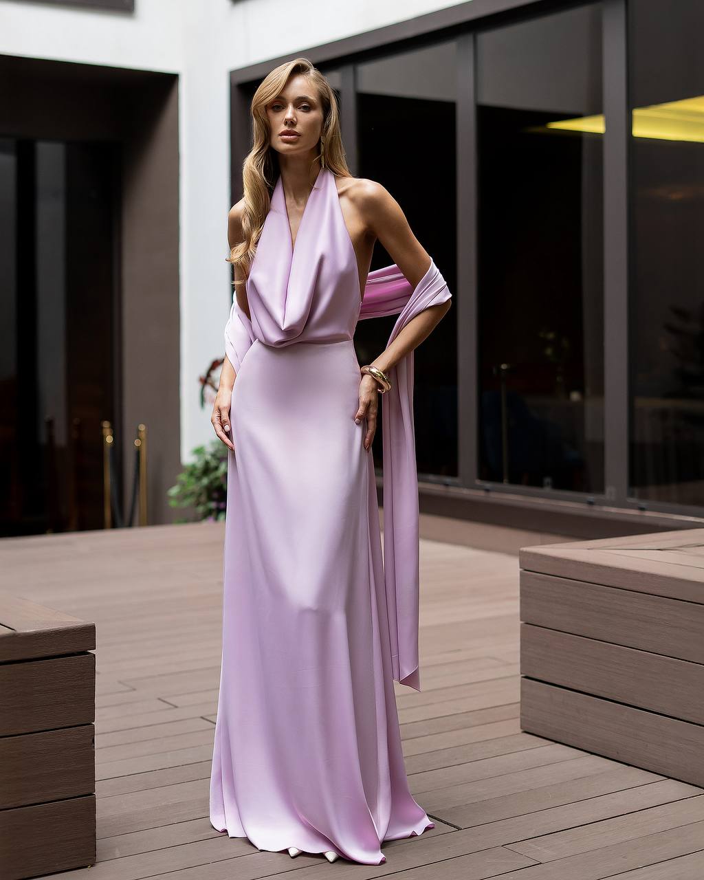 Woman in a long, light purple dress standing on a wooden deck.