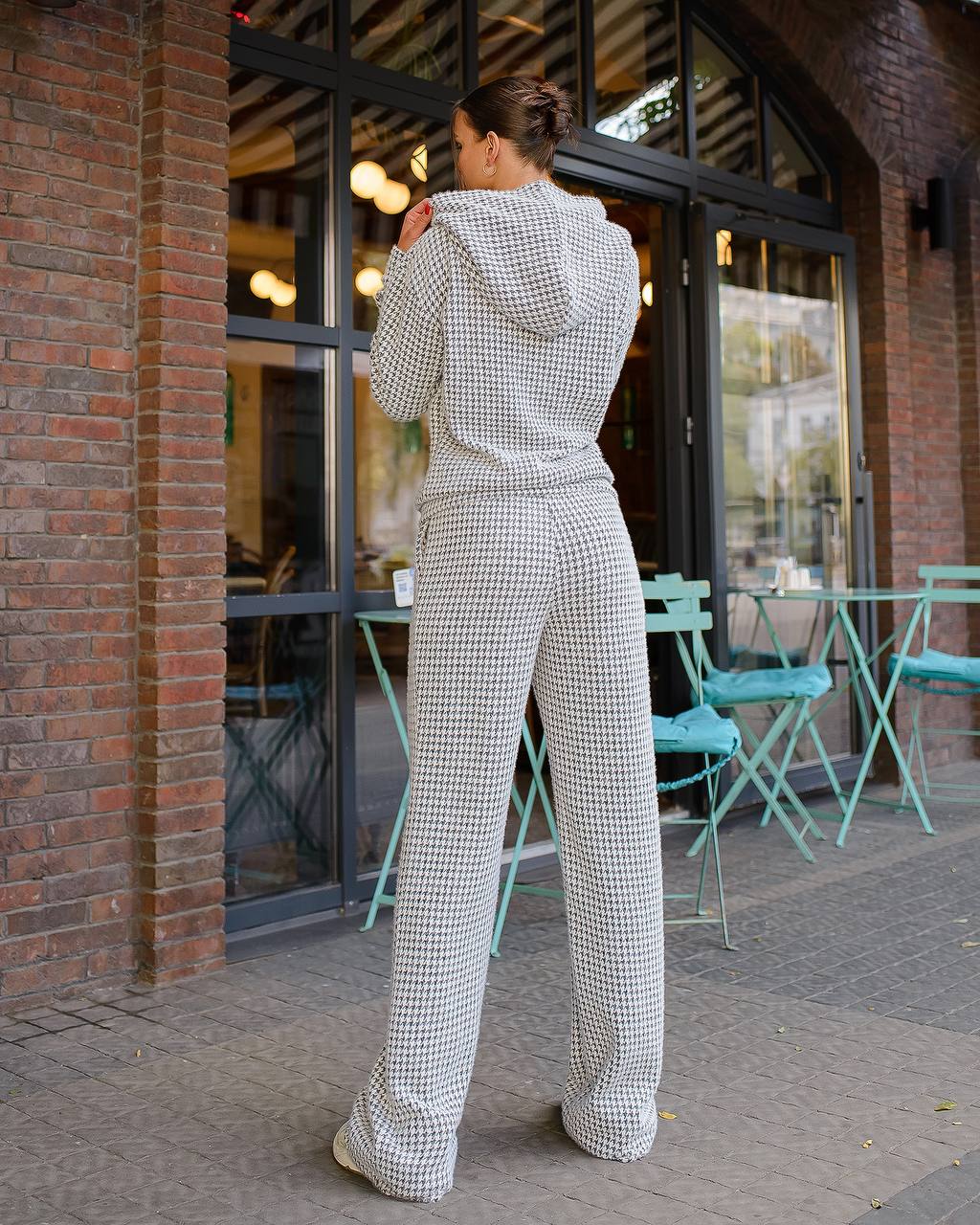 Person wearing a checkered outfit standing outside a building with tables and chairs.