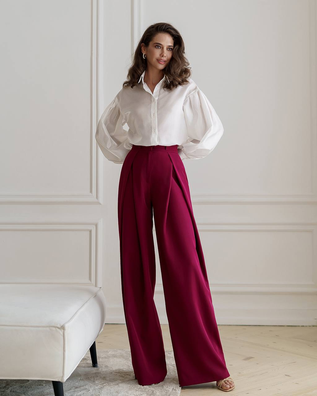 Woman wearing a white blouse and burgundy pants in an elegant room.
