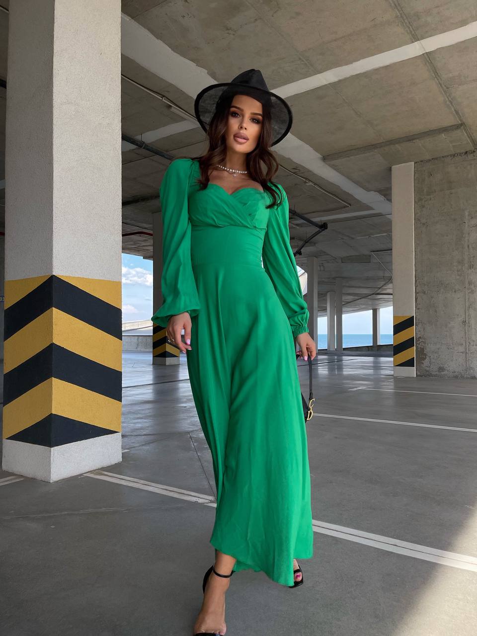 Woman in a green dress and black hat standing in an industrial setting