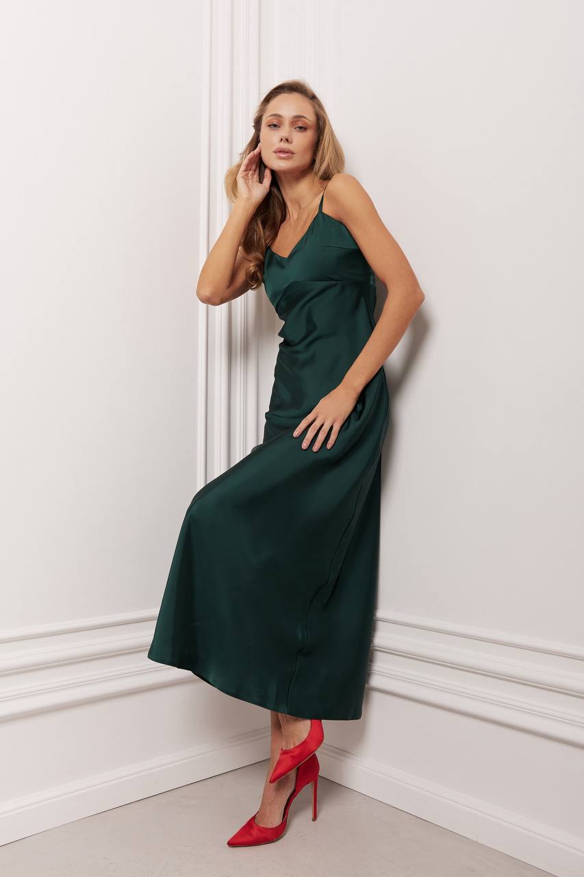 Woman in a green dress with red shoes standing against a white wall.