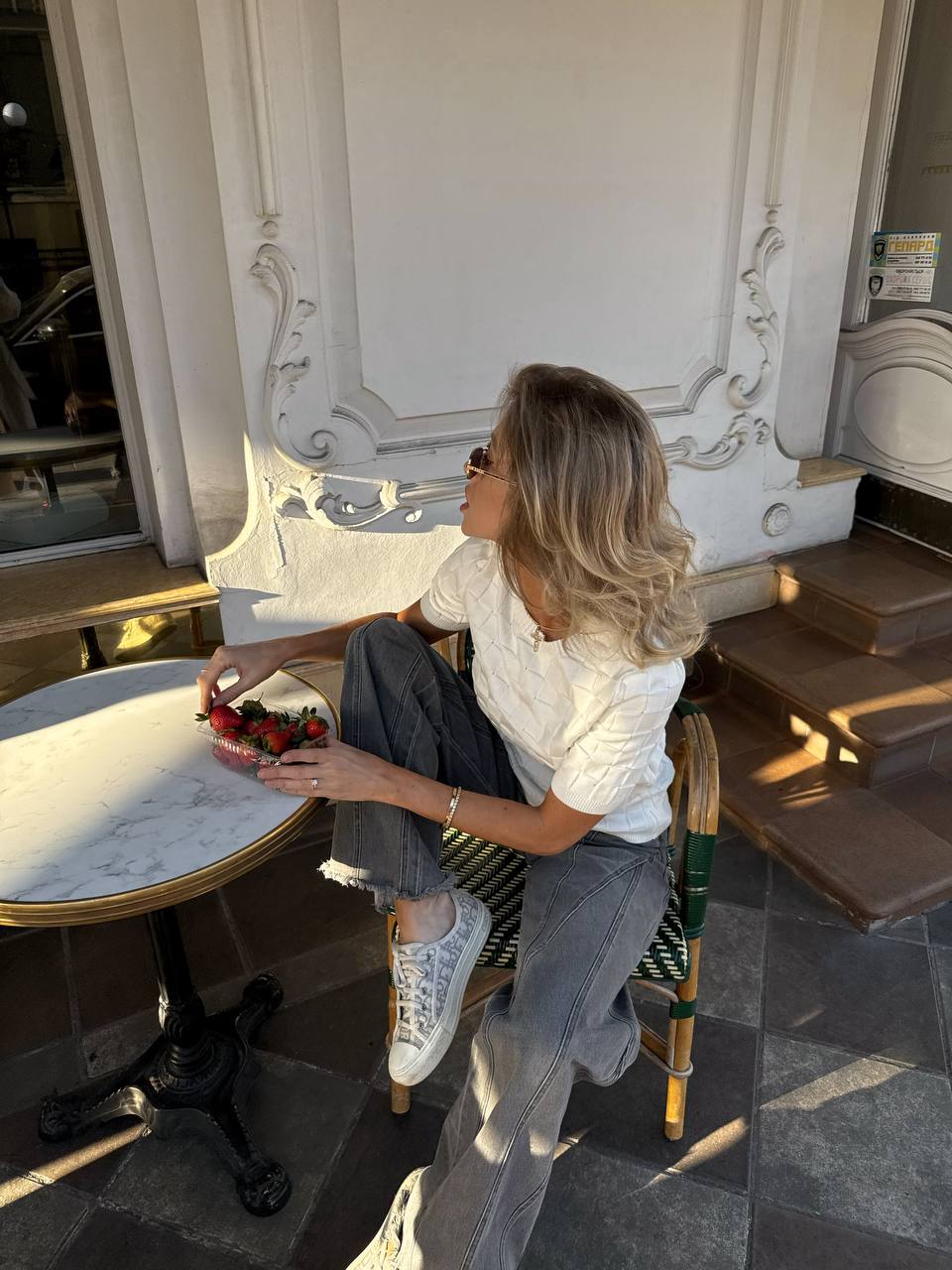 Woman sitting at a table in an elegant setting, possibly a cafe or restaurant.