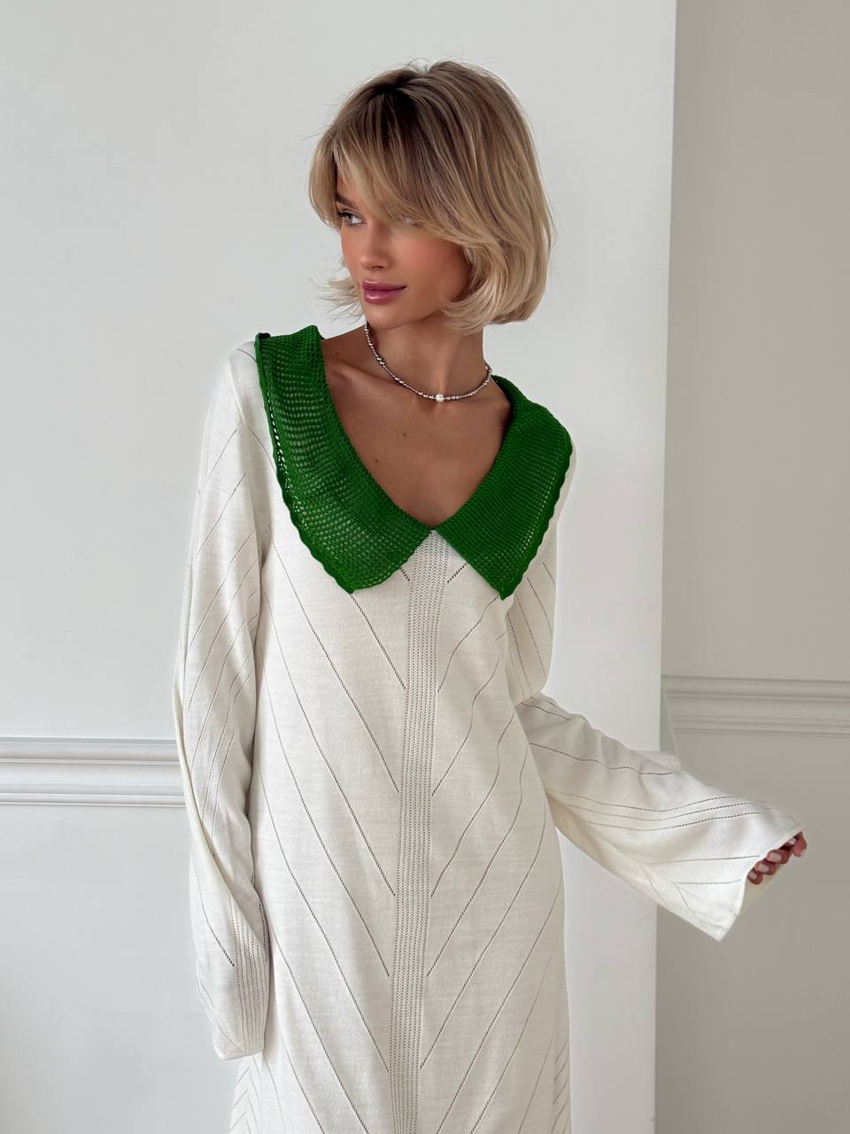 Woman wearing a white dress with a green collar against a white wall