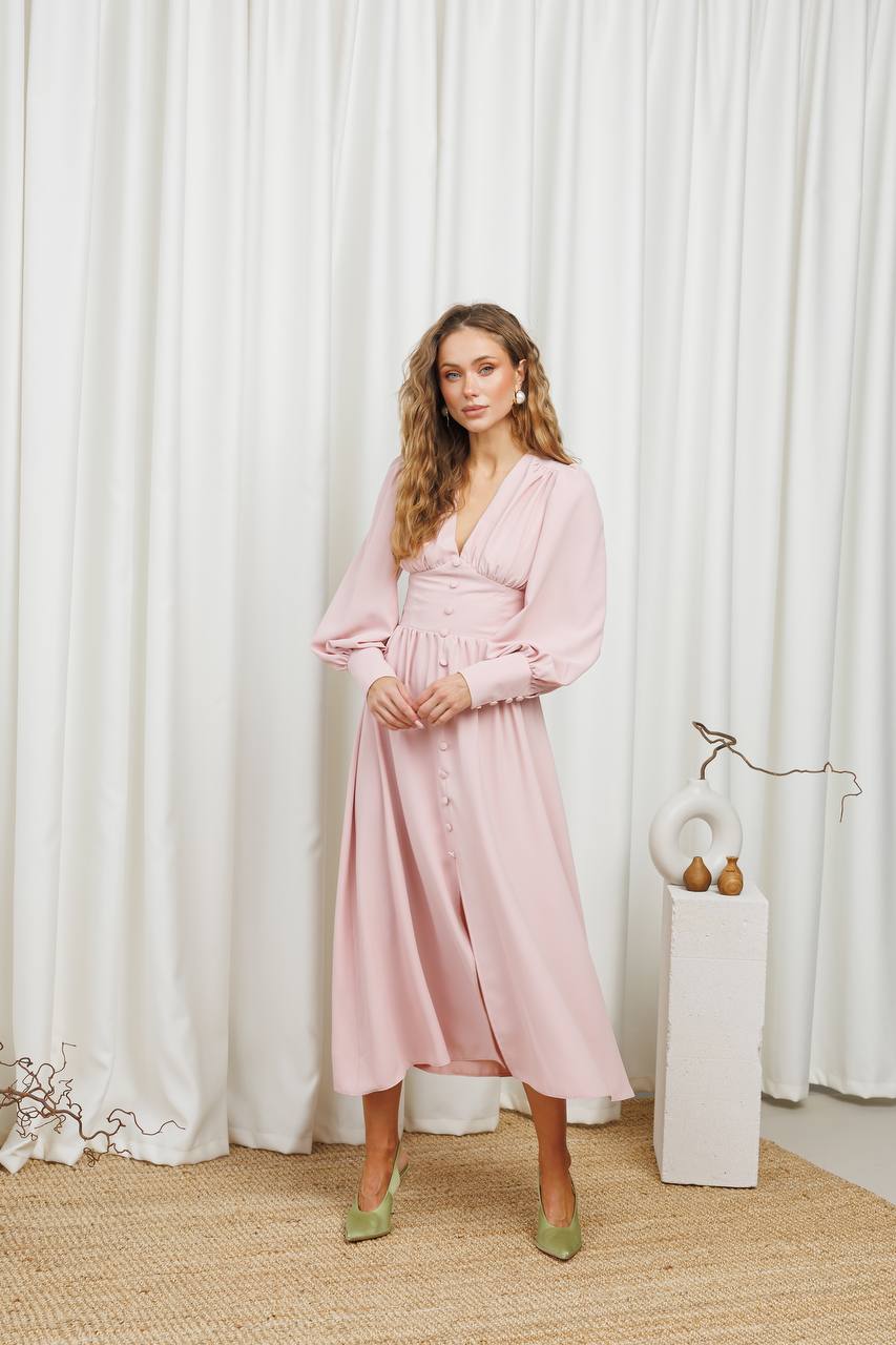 Woman wearing a pink dress standing in front of white curtains