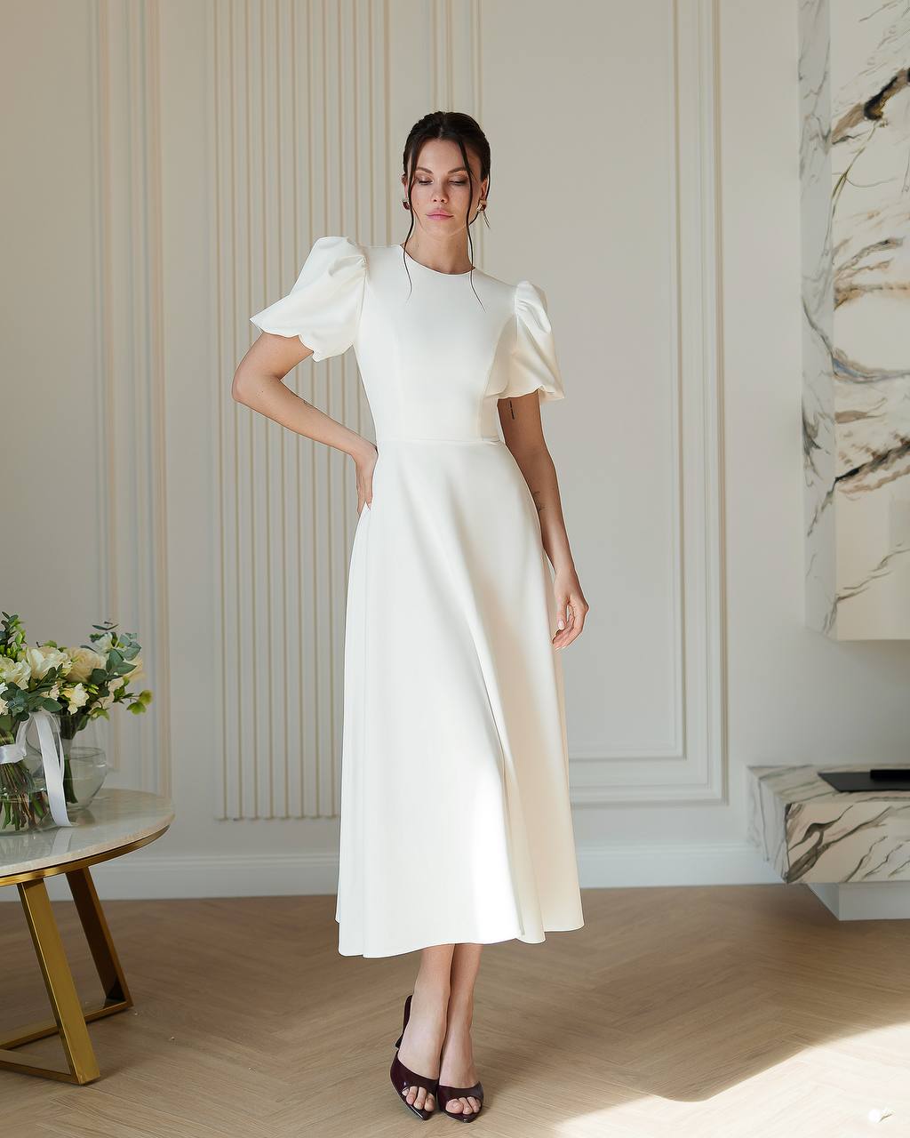 Woman wearing a white dress with puffed sleeves in an elegant room.