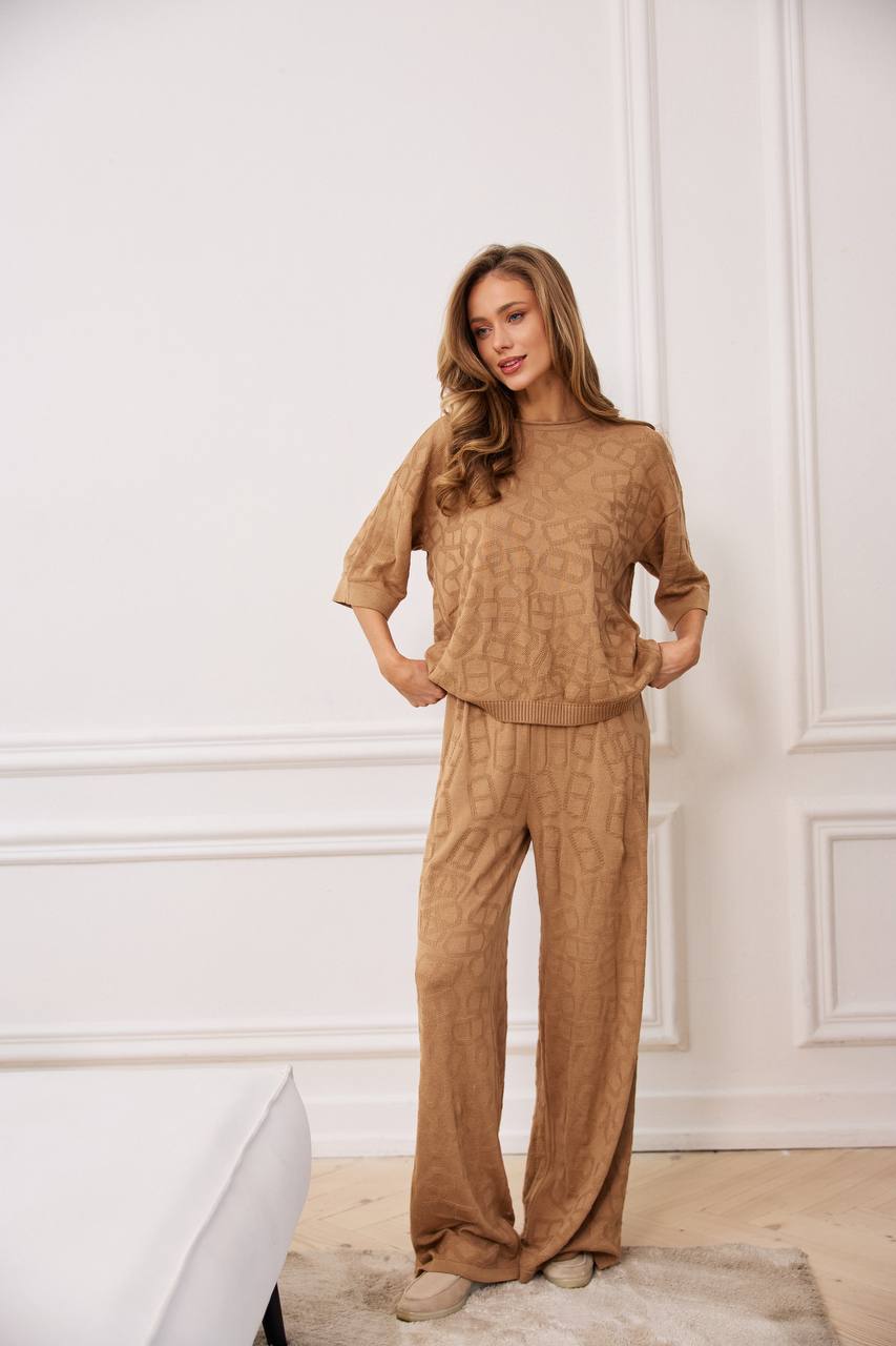 Woman wearing a brown outfit standing against a white wall.