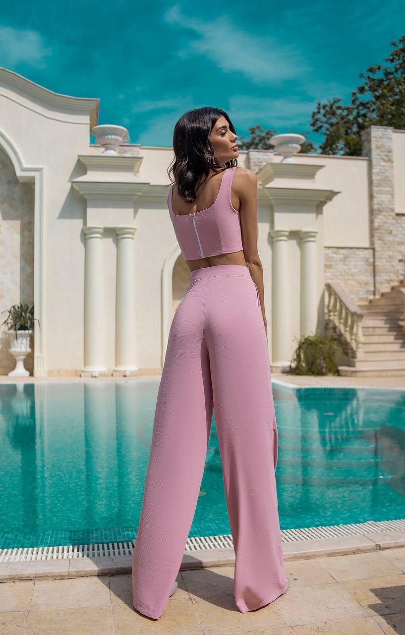 Woman in pink outfit standing by a pool with classical architecture in the background