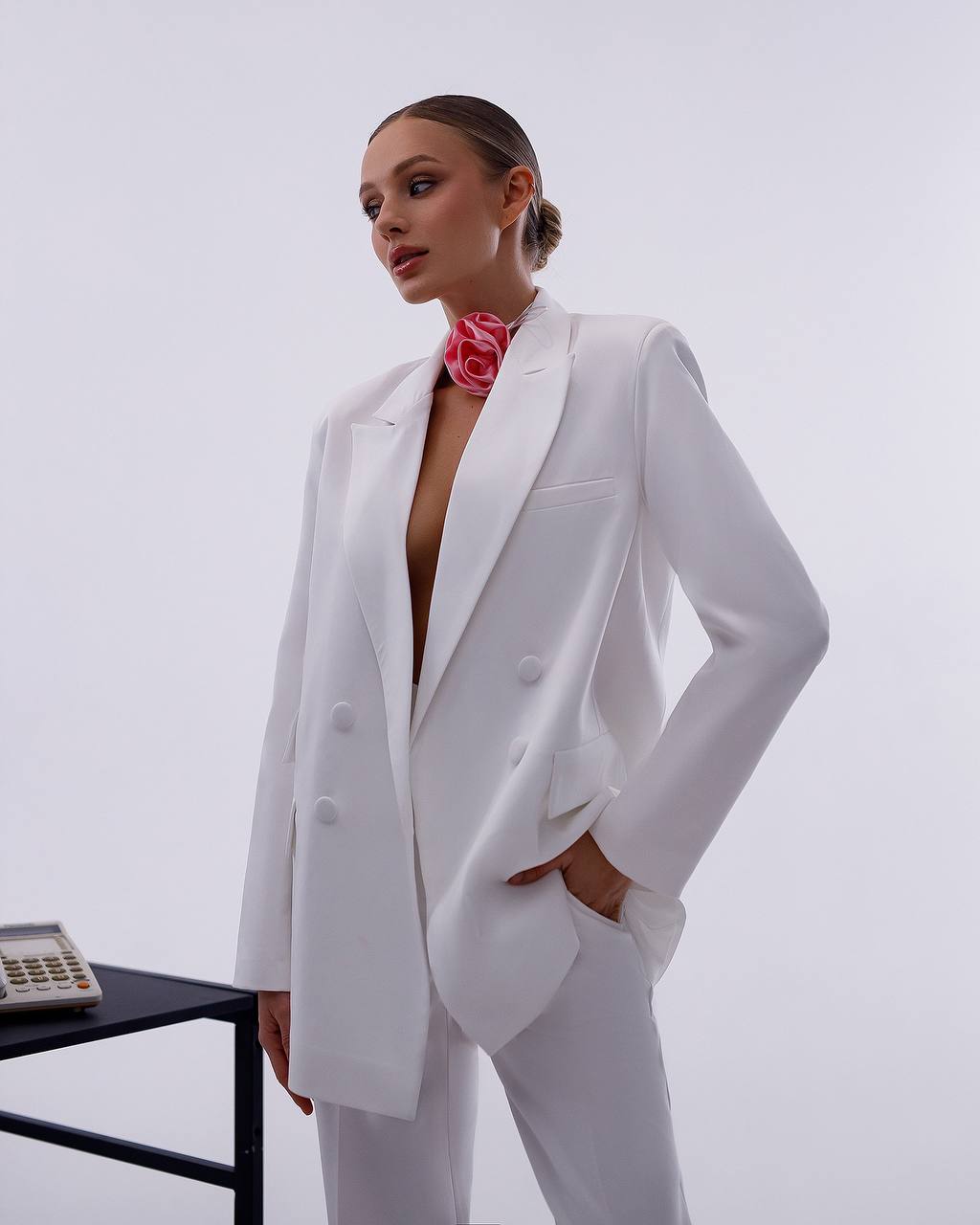 Person wearing a white suit with a pink scarf against a light gray background