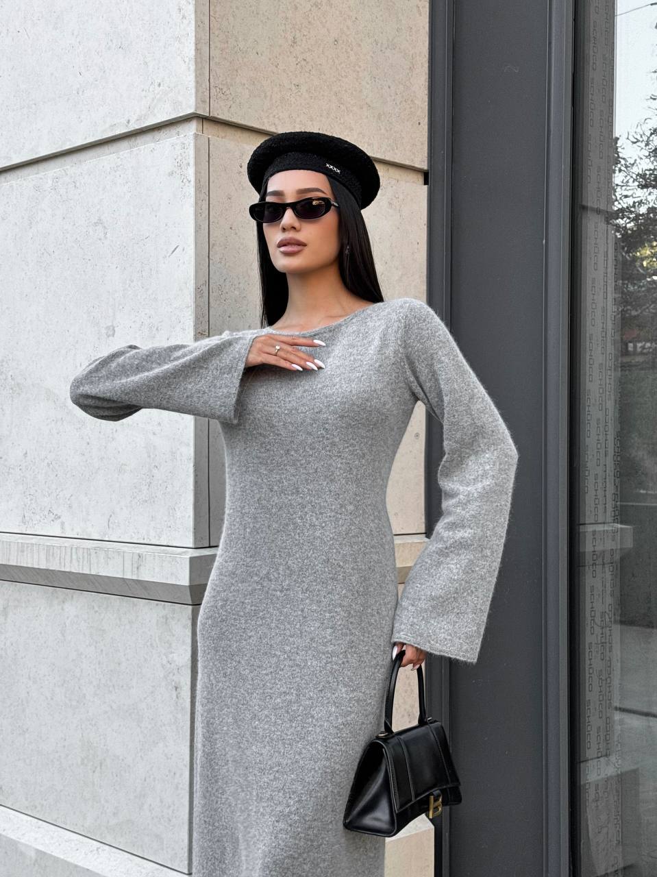 Woman in a gray dress and black beret standing against a building.