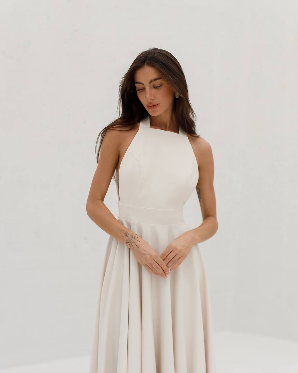 Woman wearing a white halter neck dress against a plain background