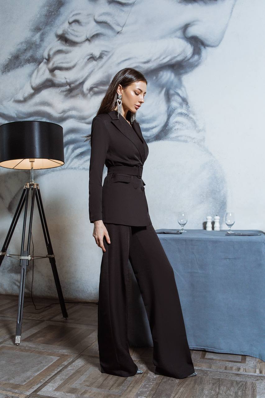 Woman in a black outfit standing in a room with a lamp and table.