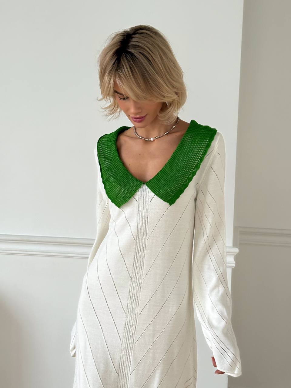 Woman wearing a white dress with a green collar against a plain background
