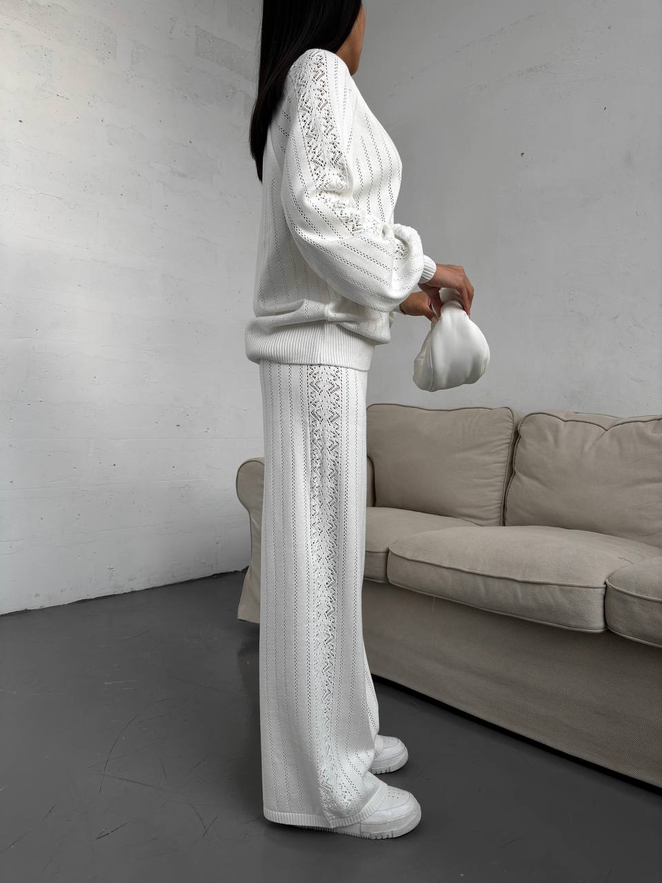 Person wearing a white outfit with lace details in a minimalistic room.