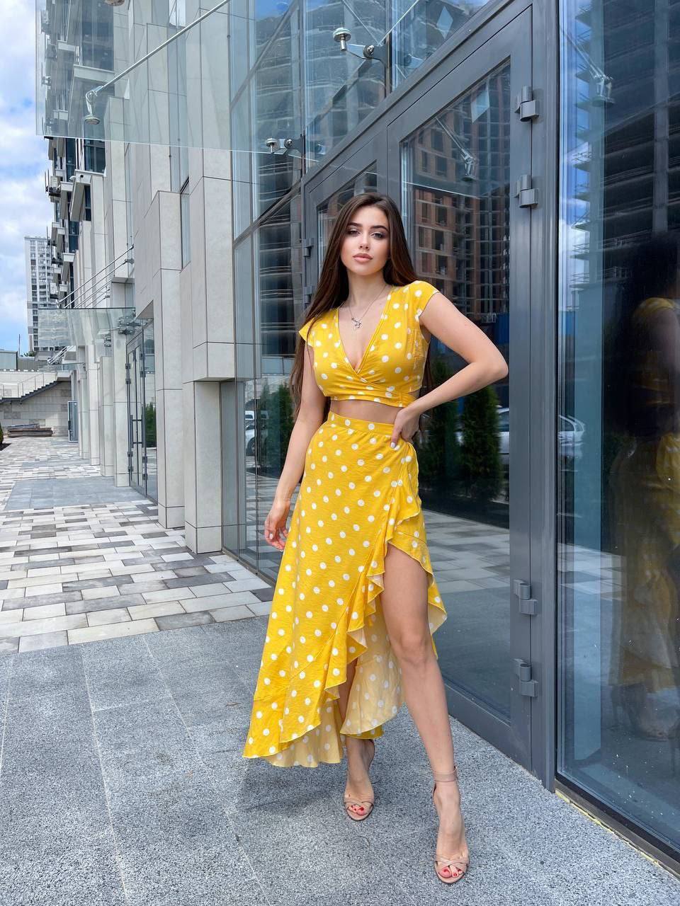 Woman in a yellow polka dot dress standing in front of a modern building.