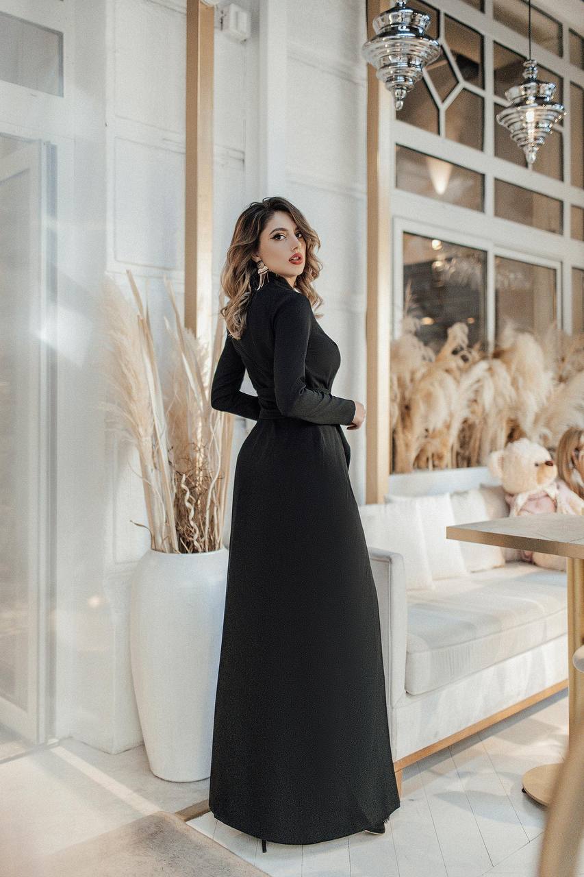 Woman in a black dress standing in a stylish interior setting with decor elements.