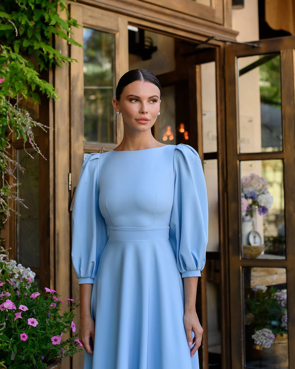 Woman in a light blue dress standing in front of a wooden door with floral decorations.
