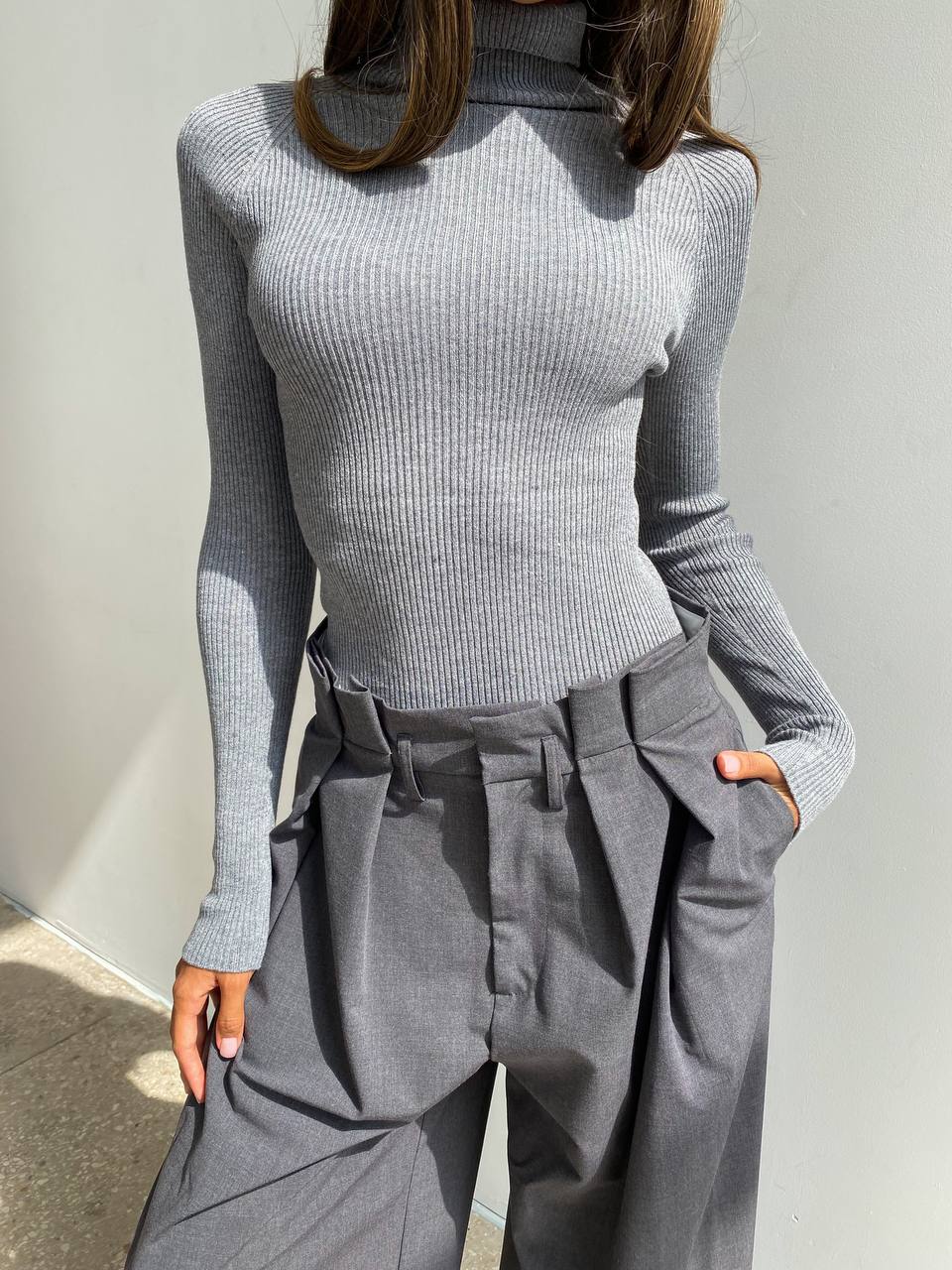 Person wearing a gray ribbed turtleneck sweater and gray high-waisted pants against a light gray background.