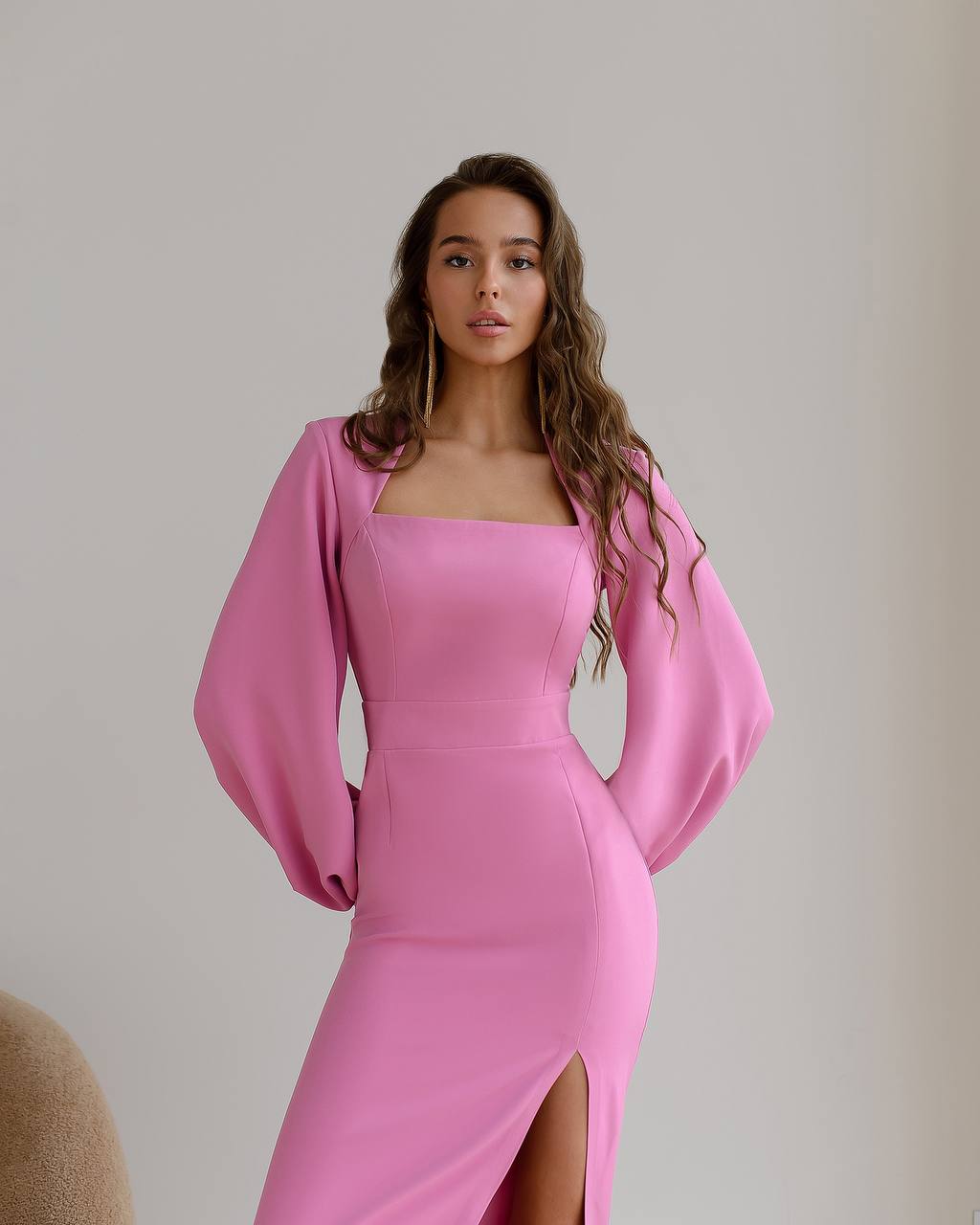 Woman wearing a pink dress with wide sleeves against a plain background