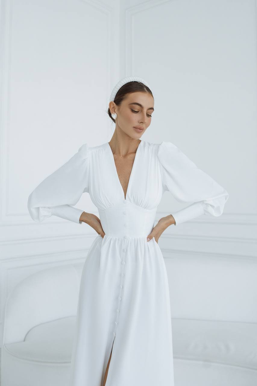 Woman wearing a white dress with long sleeves against a white background