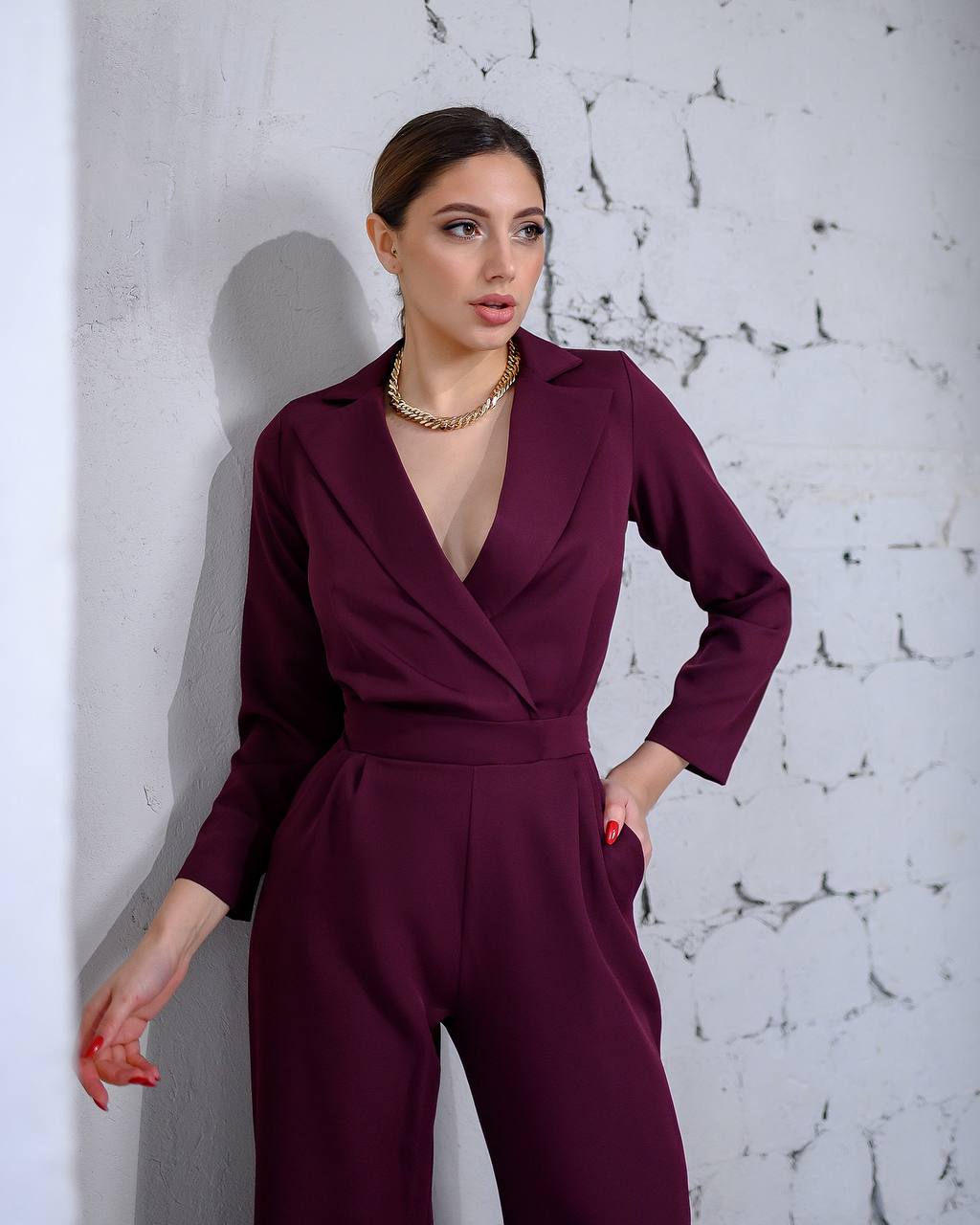 Woman wearing a burgundy jumpsuit against a textured white wall