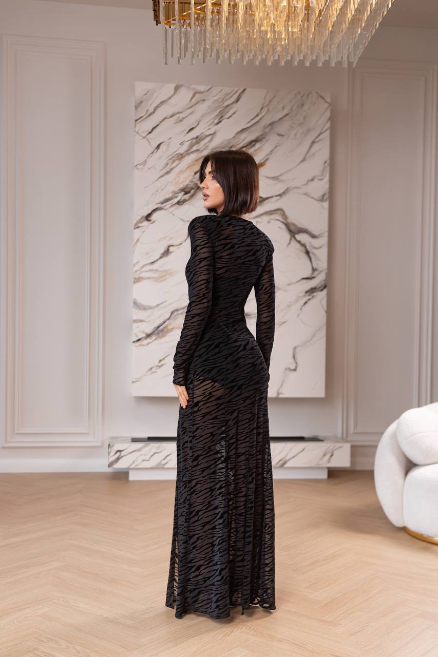 Woman in a black dress standing in a stylish room with marble wall art and chandelier.