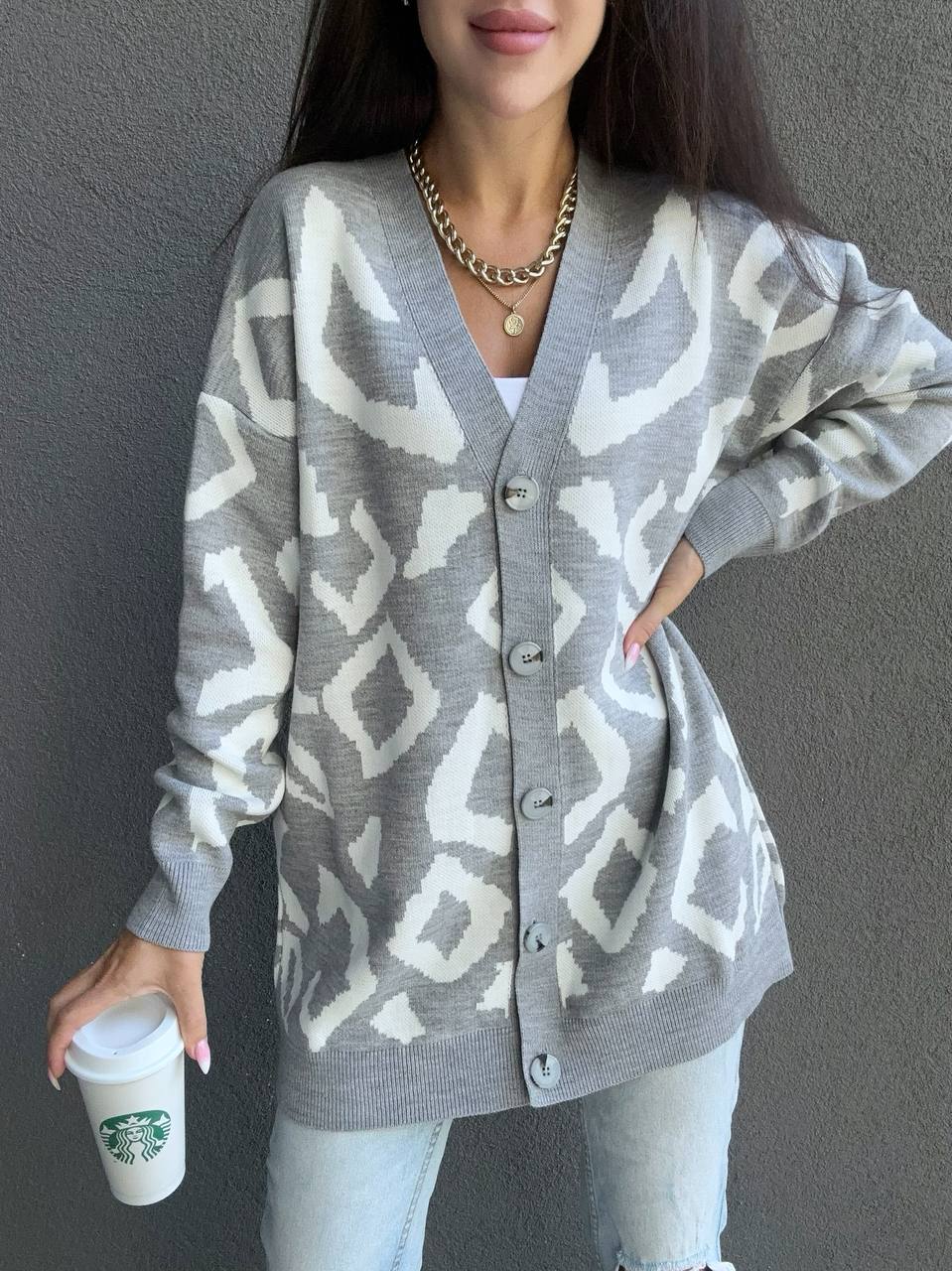Person wearing a gray cardigan with white geometric pattern, holding a Starbucks cup against a plain background