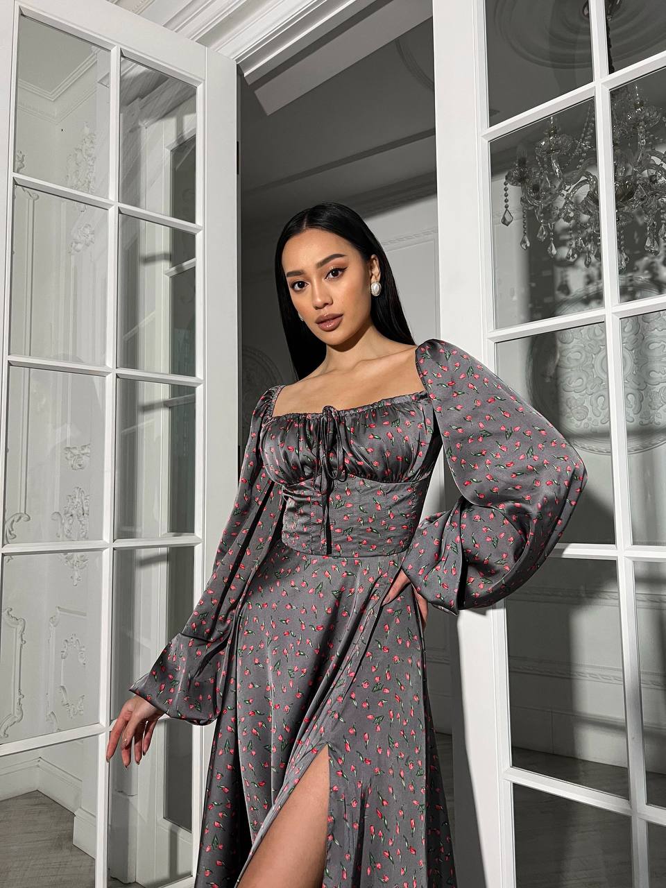 Woman wearing a gray patterned dress with long sleeves in a room with large windows.