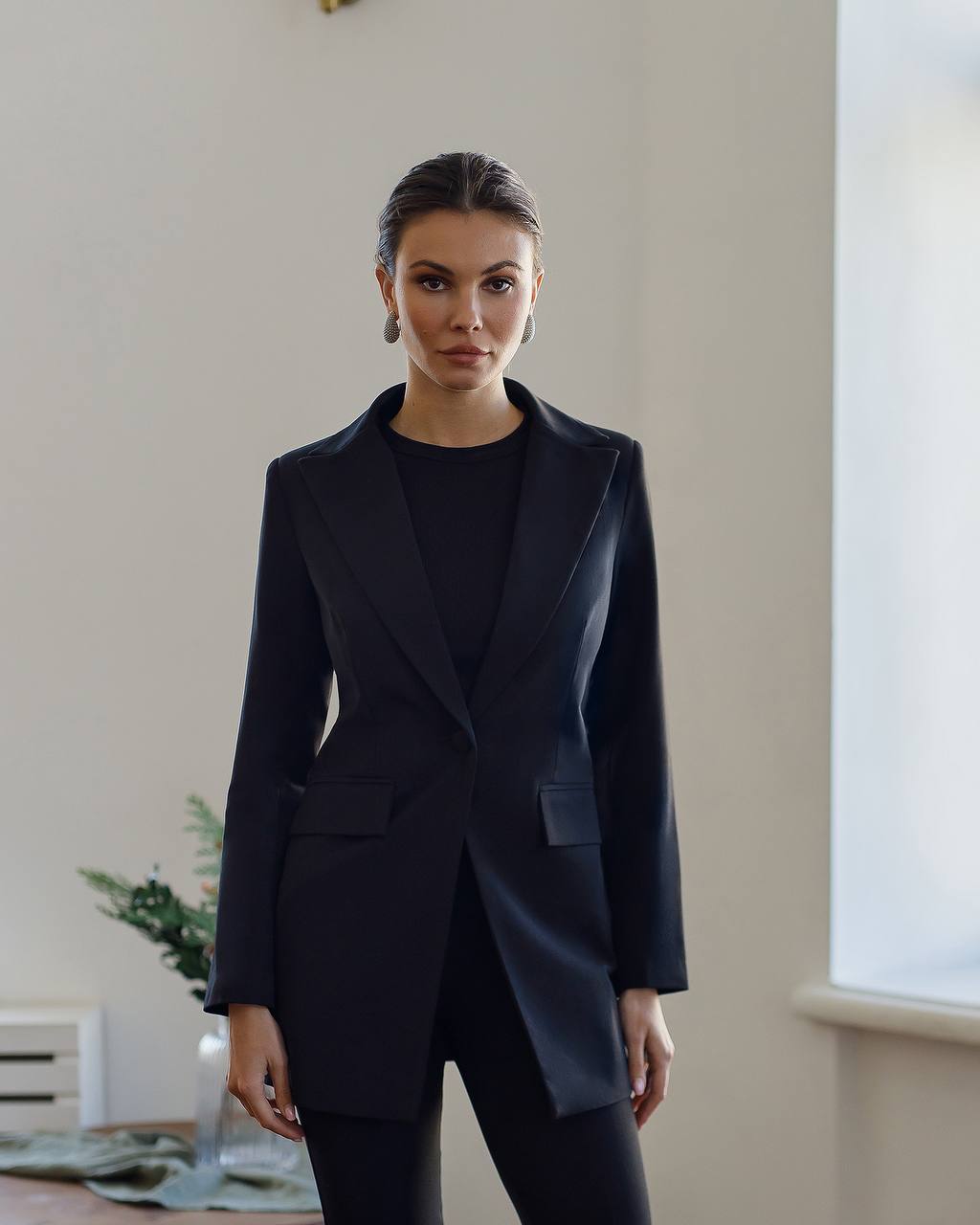 Woman wearing a dark blue suit standing indoors with a neutral background