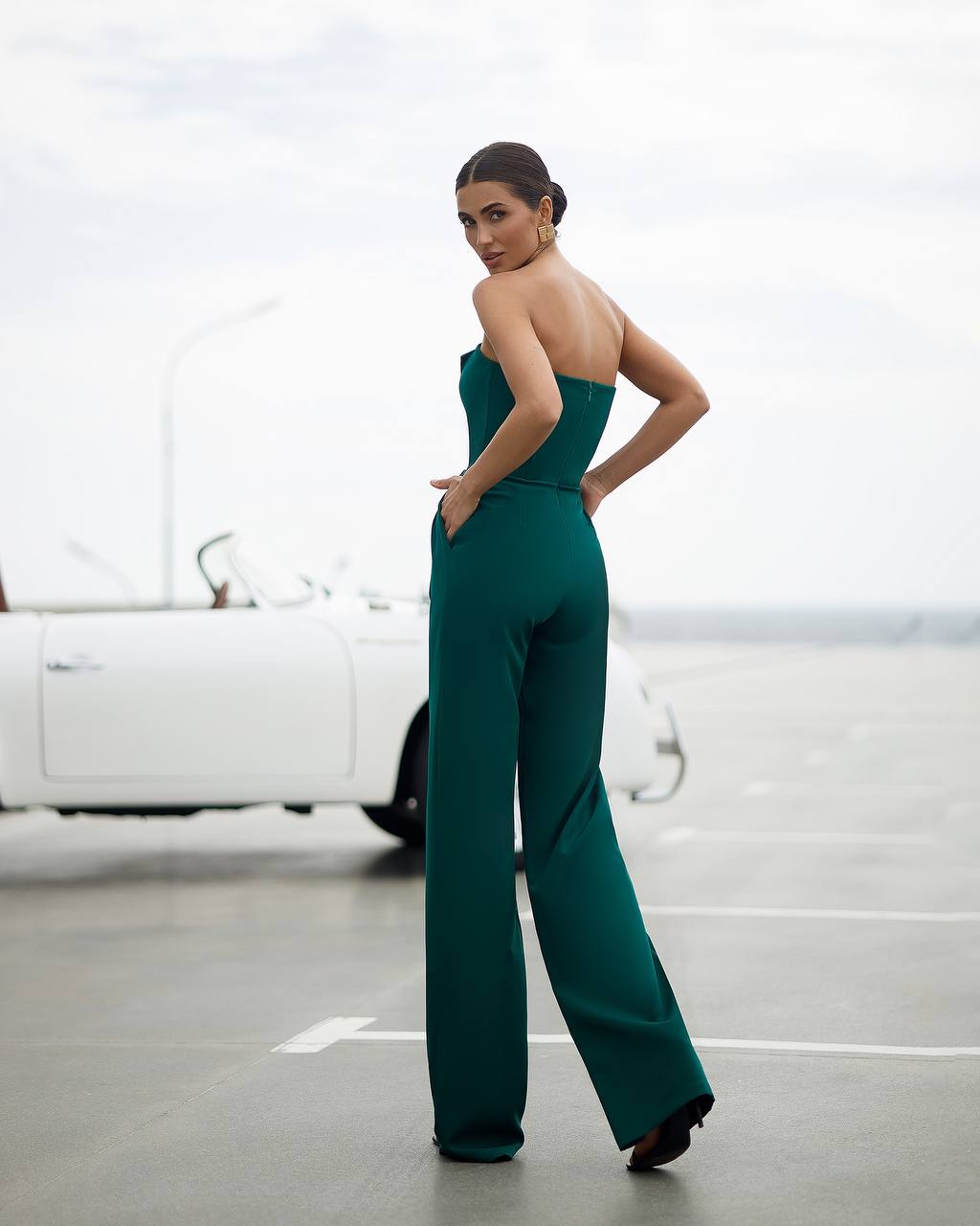 Woman in a green strapless jumpsuit standing in a parking lot.