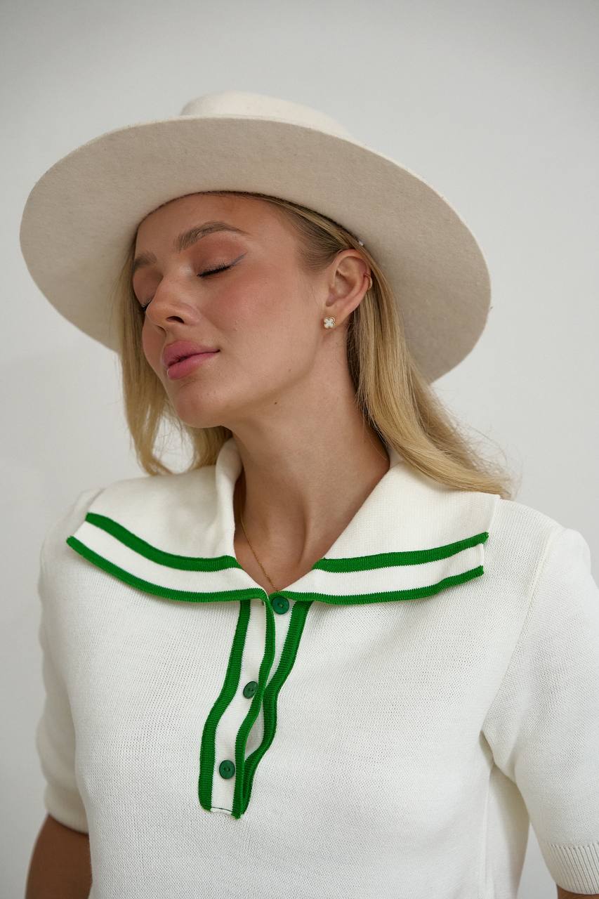 Woman wearing a white outfit with green accents and a beige hat against a plain background