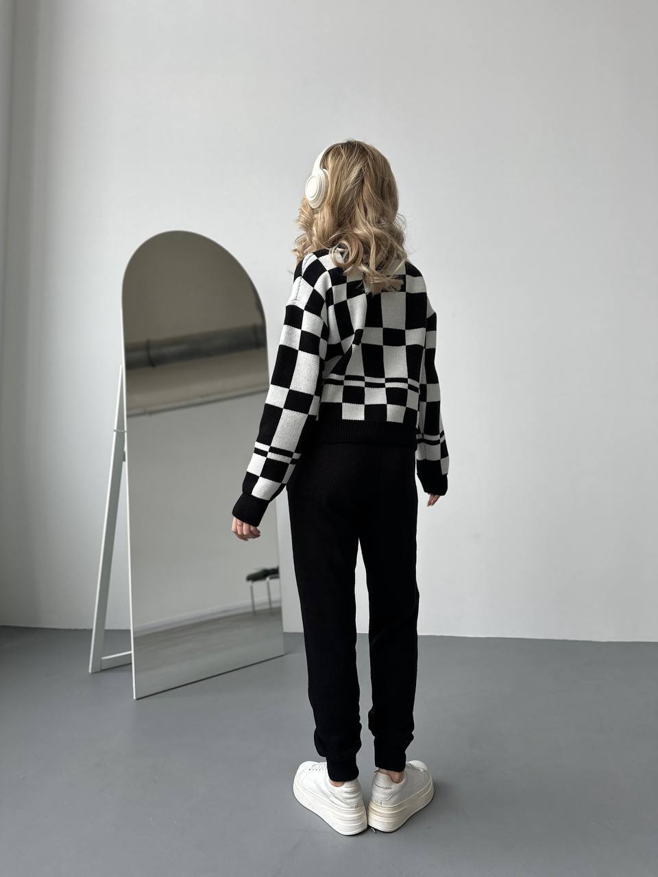 Person wearing a black and white checkered sweater and black pants standing in front of a mirror.
