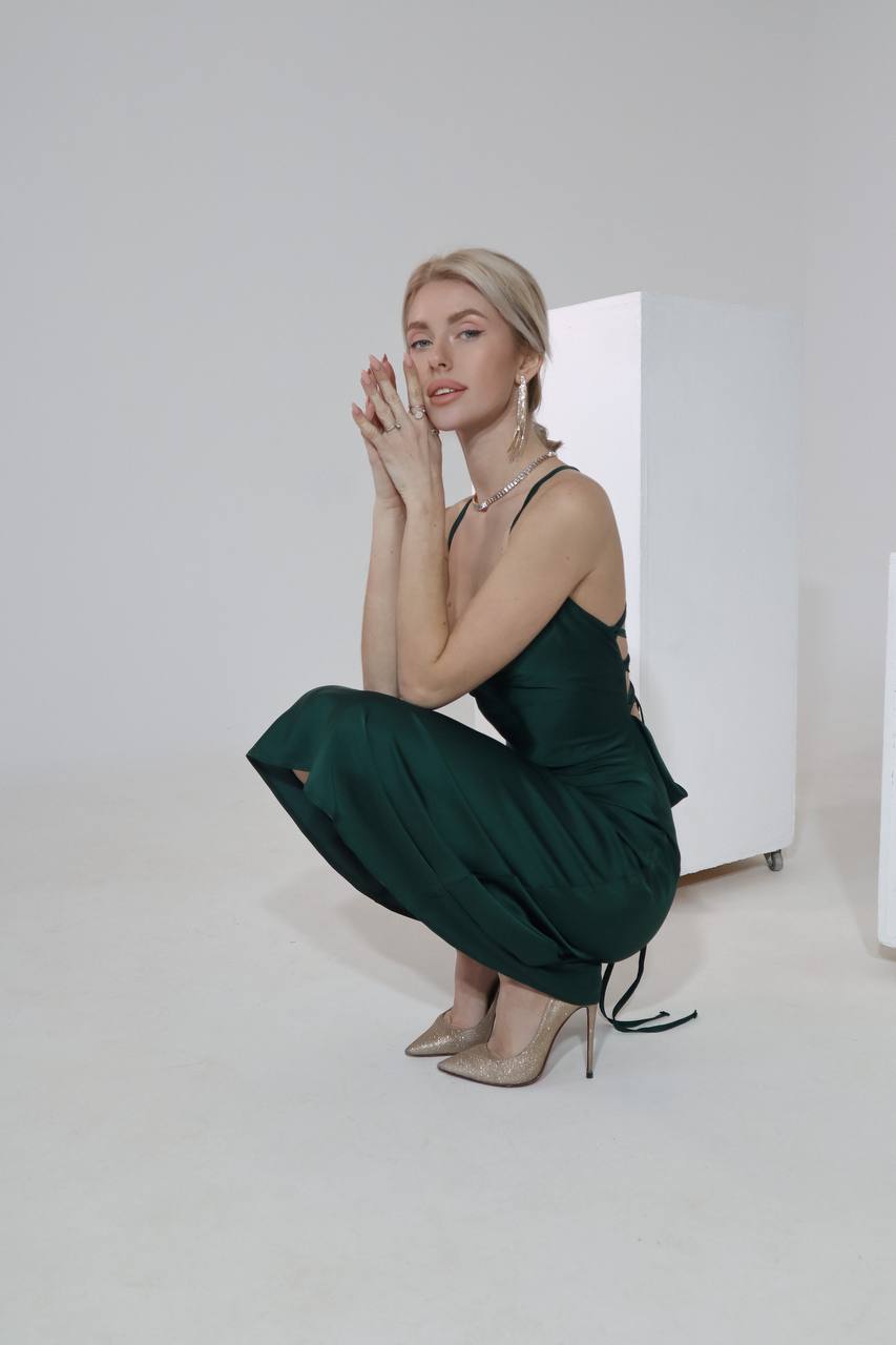 Woman in a green dress sitting on a white floor with a white wall background