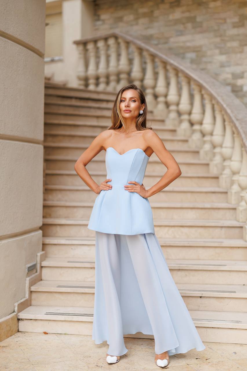 Woman in a light blue strapless top and flowing pants standing on stone steps.