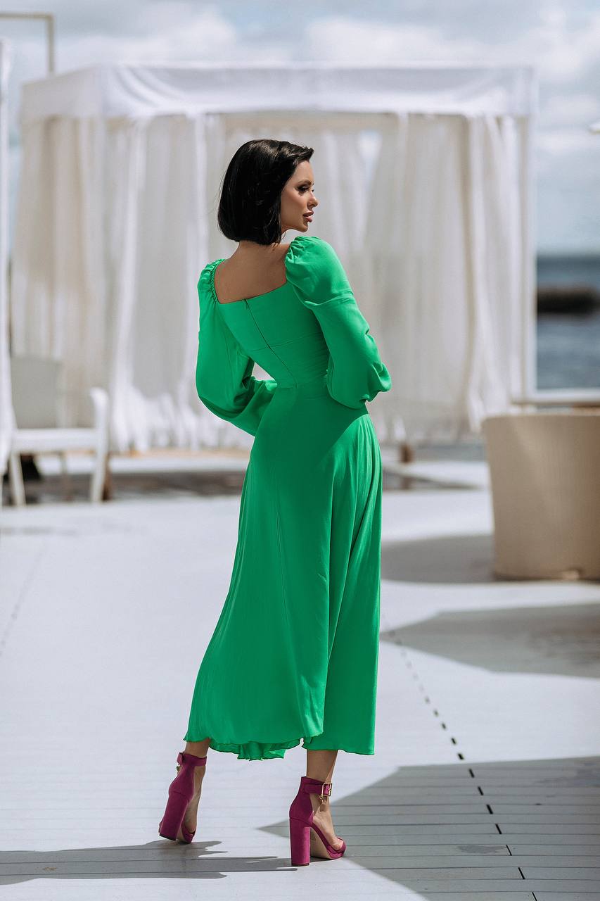 Woman in a green dress standing on a sunlit deck with white chairs and a cloudy sky.
